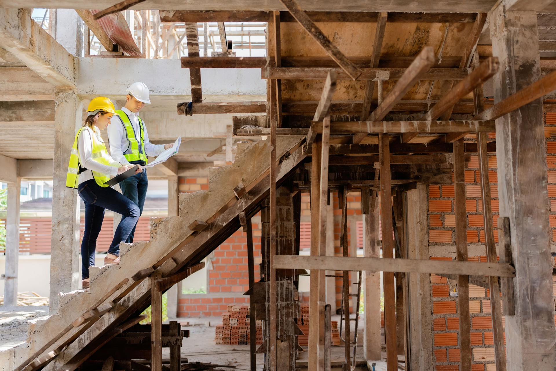 Two Asian male and female engineers looking at blueprints and listnotes. walking on stairs in the design of construction work about architecture For future industries, wear vests and helmets.